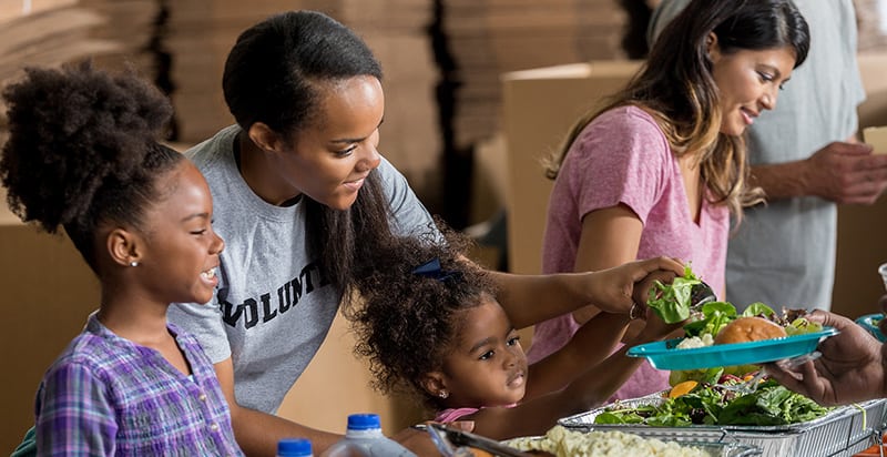Volunteers, including a young child, engaged in feeding people, reflecting the blog's exploration of hunger in America and where to find help.