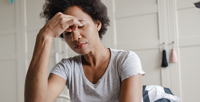 An image of a fatigued woman pinching the bridge of her nose, representing the challenges of treatment fatigue in rehabilitative and therapeutic settings, including drug and alcohol rehabs and reentry programs.
