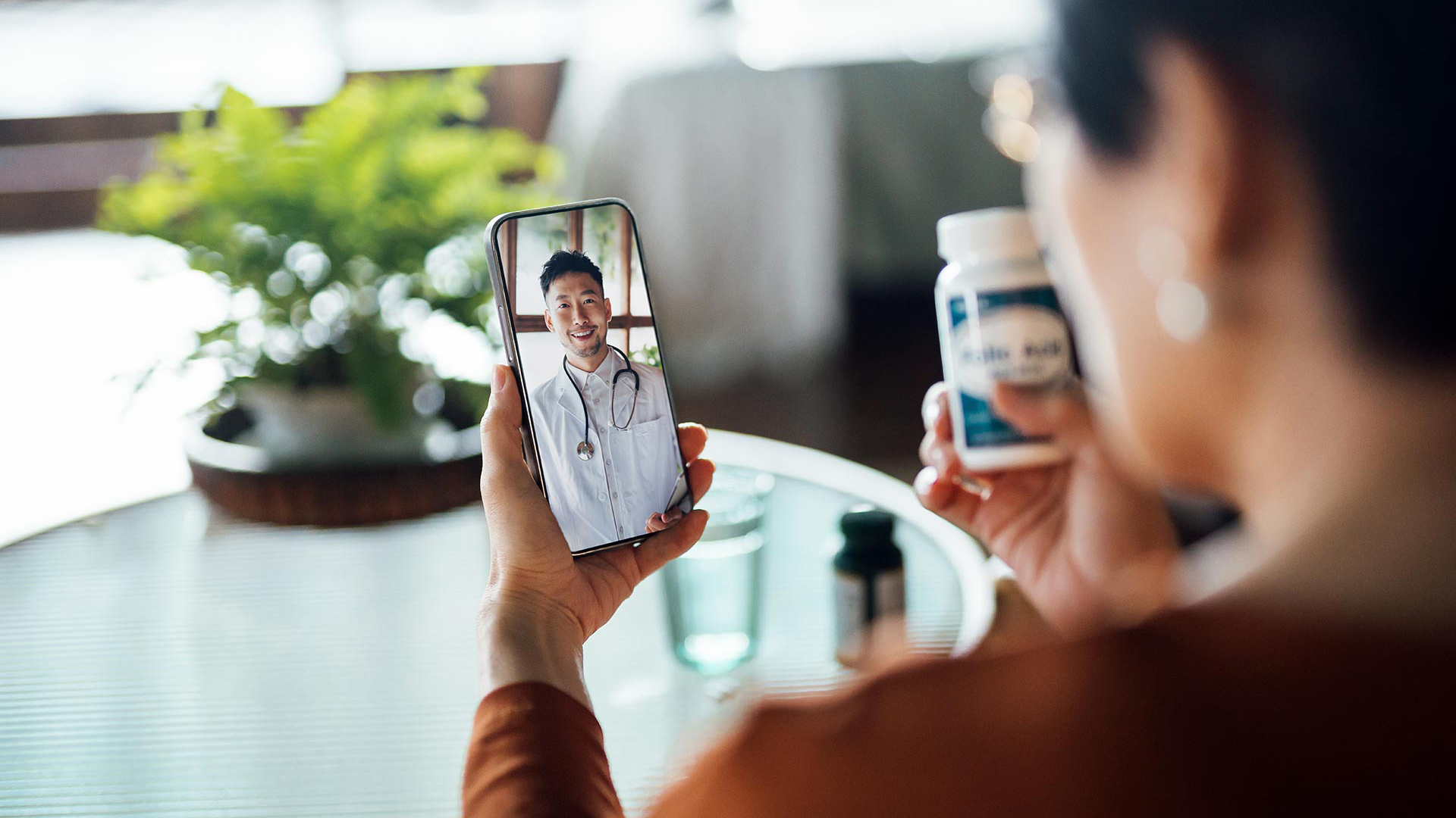A woman holds a pill bottle in one hand and a smartphone with a virtual doctor on screen in the other, illustrating how formerly incarcerated individuals can embrace technology for accessible healthcare solutions.