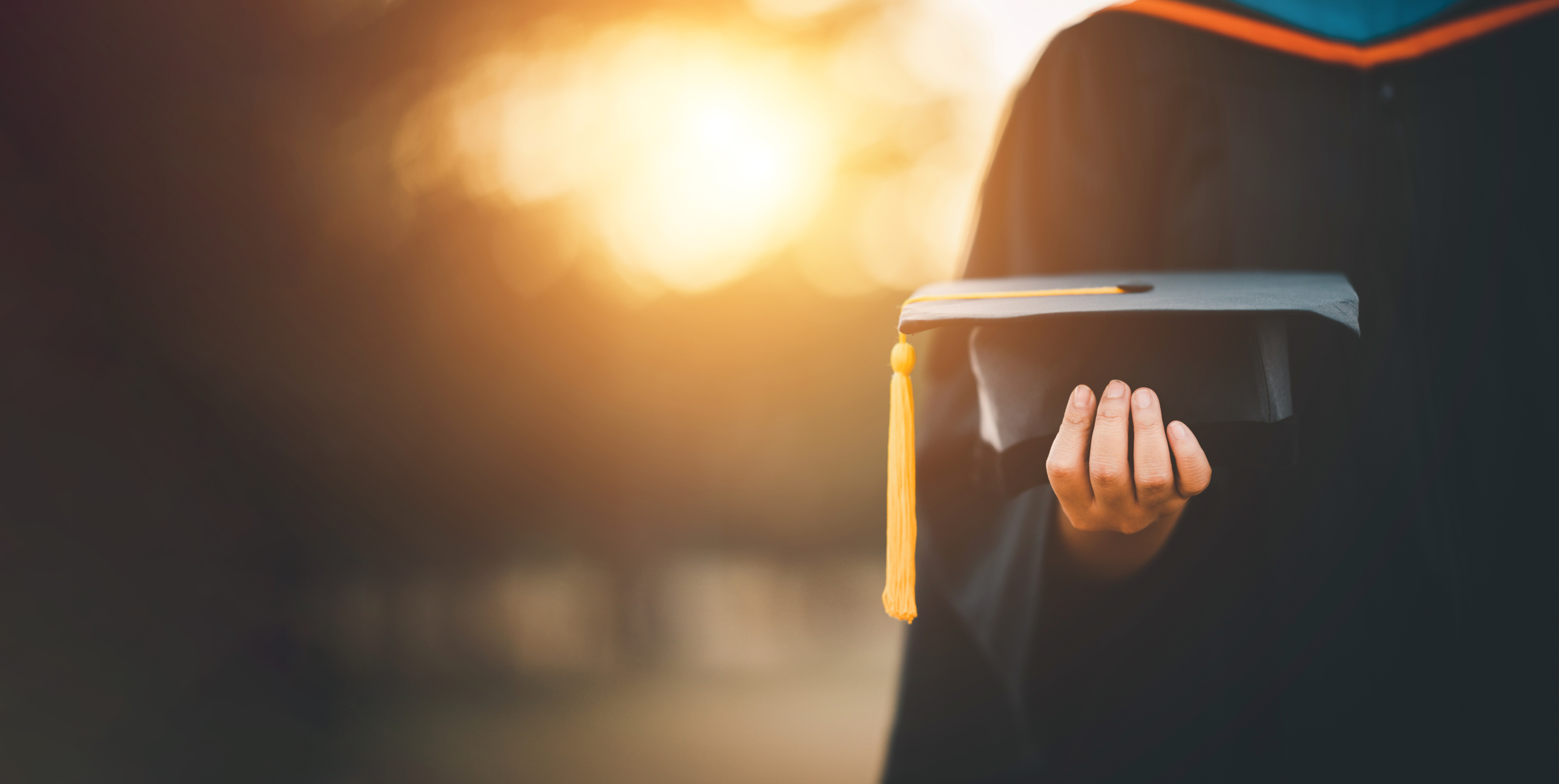 A woman in a graduation robe holds her cap, embodying the narrative of formerly incarcerated individuals pursuing higher education, breaking barriers and embracing a new chapter.