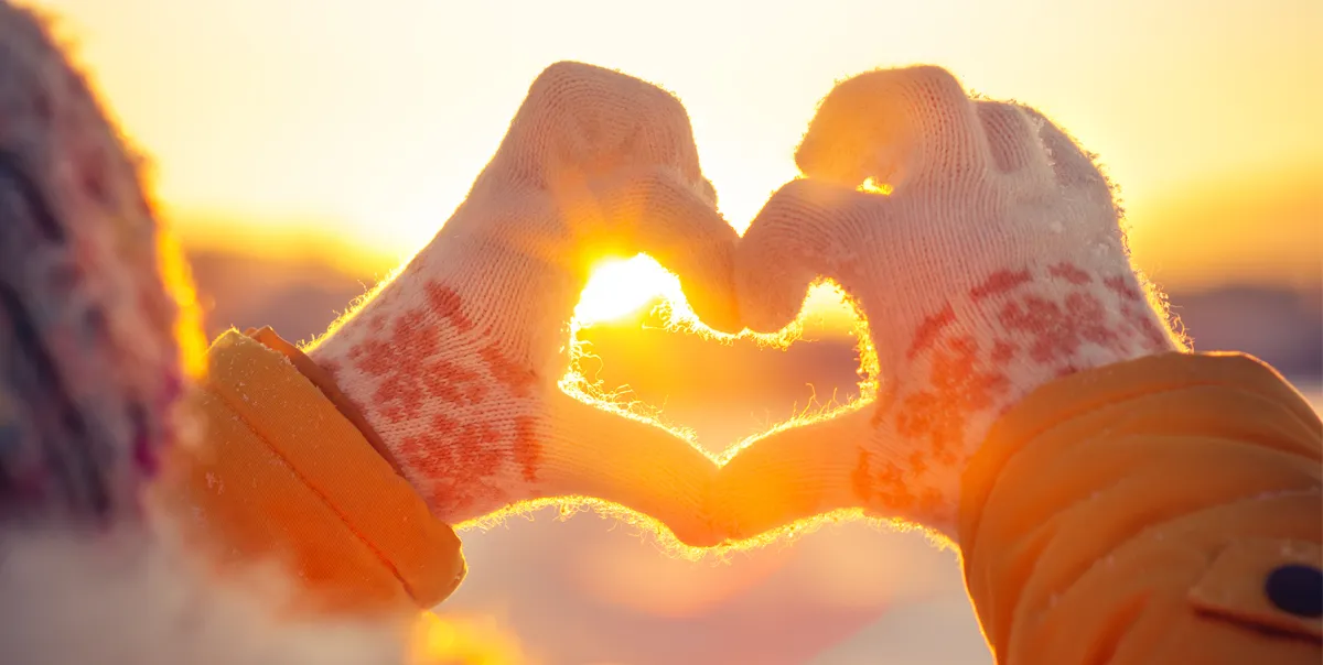 Two hands in winter gloves create a heart over a sunrise, echoing the longing of the formerly incarcerated separated from family during the holidays.