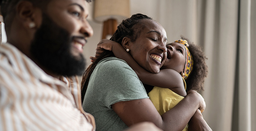 A smiling couple and their young daughter embrace joyfully after reuniting through transitional housing support.