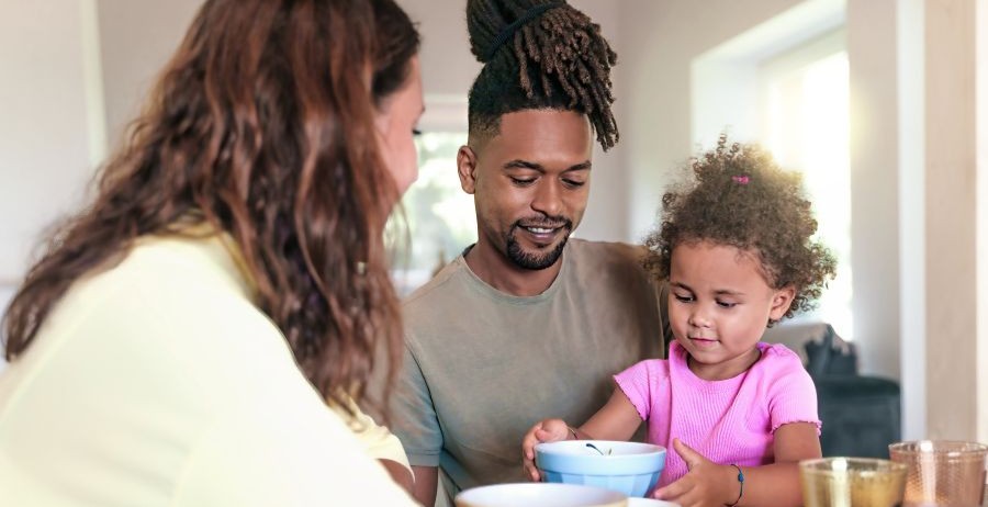 Man and woman sitting at a dining room table with their young daughter nearby, focusing on family finances and child support payments.