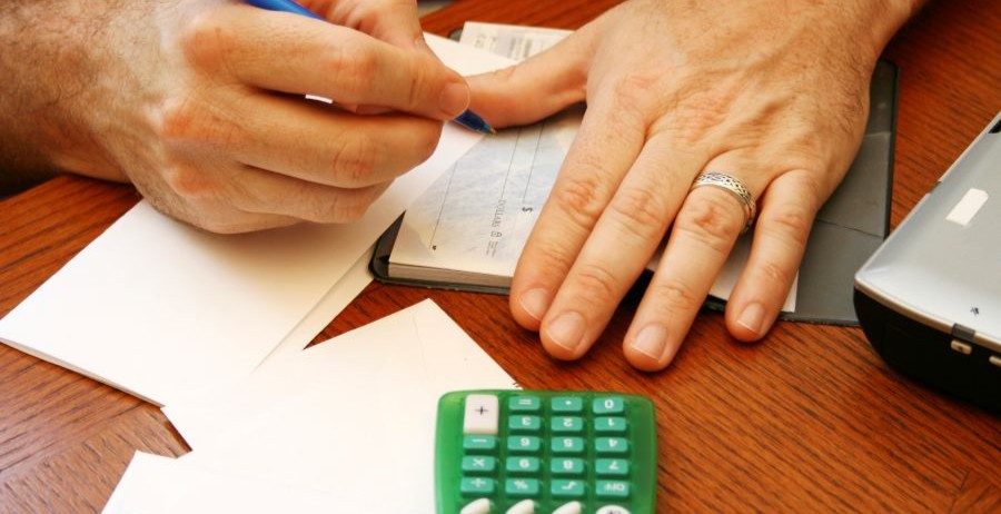 Man’s hands writing a check with a calculator and envelopes nearby, focusing on credit building and managing finances.