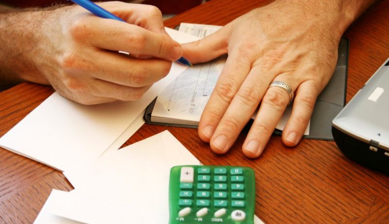 Man’s hands writing a check with a calculator and envelopes nearby, focusing on credit building and managing finances.