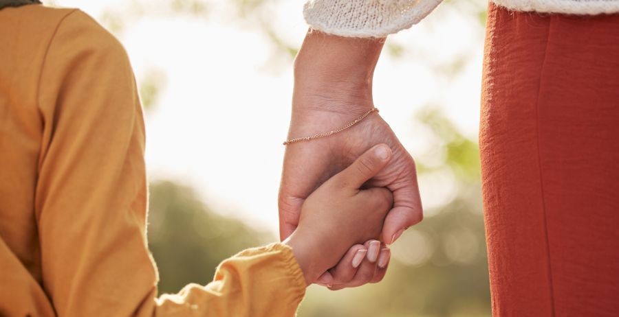 Mother and child holding hands in a sunny park, showing support and connection for families with incarcerated parents.